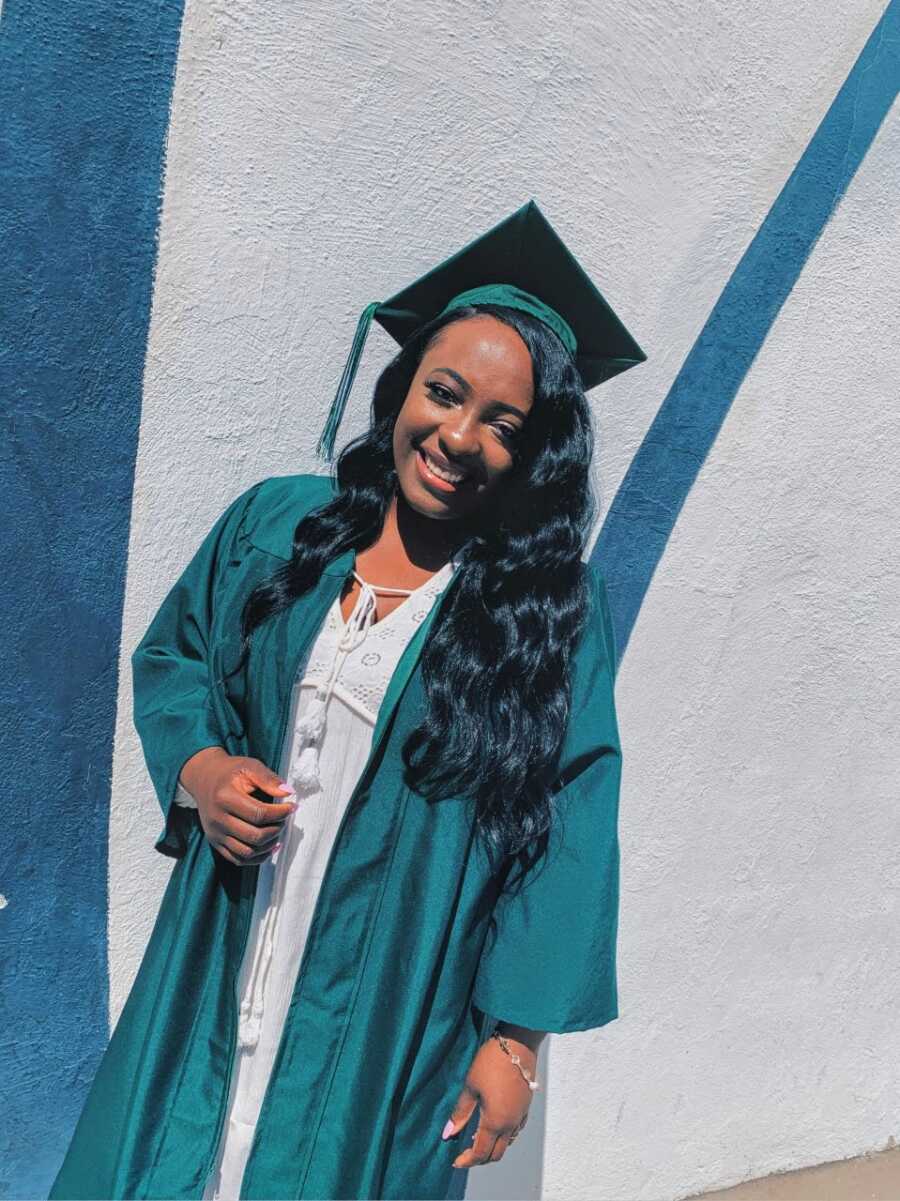 Young girl takes a photo in her graduation cap and gown with a white dress on underneath