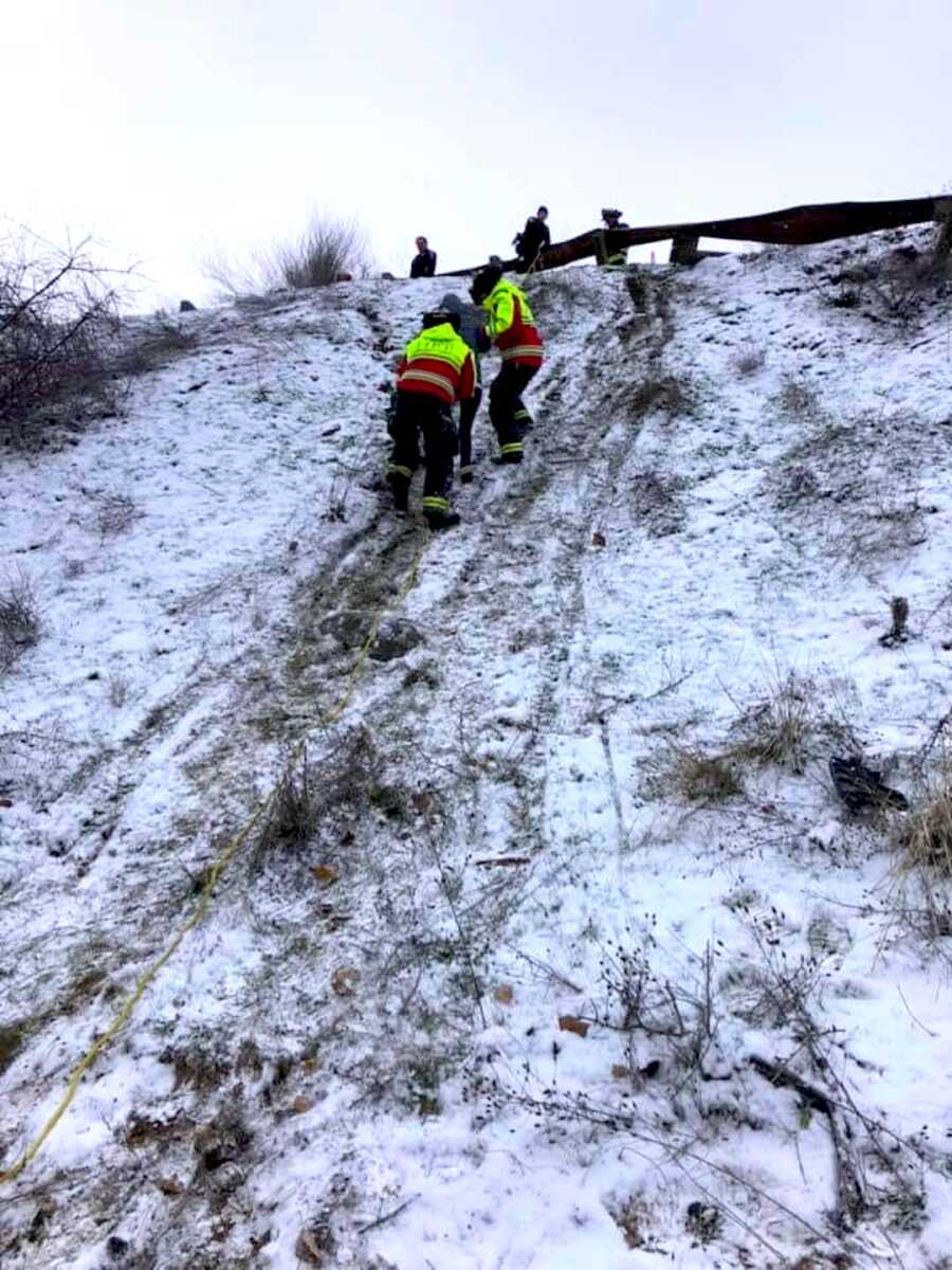 two rescue workers bringing a pregnant woman who crashed her car down a hill back up the hill to bring her to safety