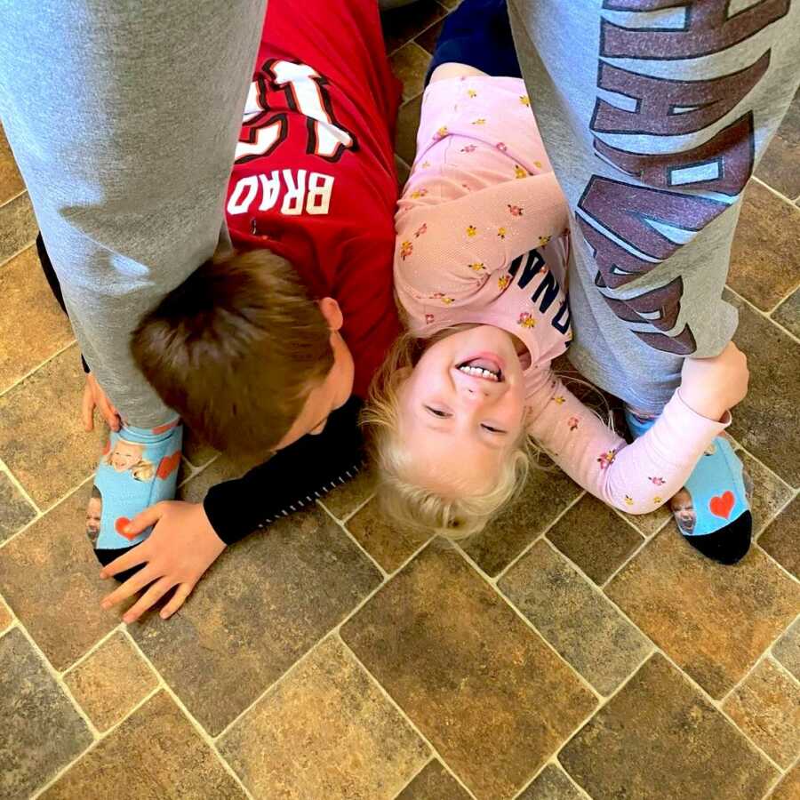 two children, son and daughter, lay on the floor between their mom's legs grabbing her ankles