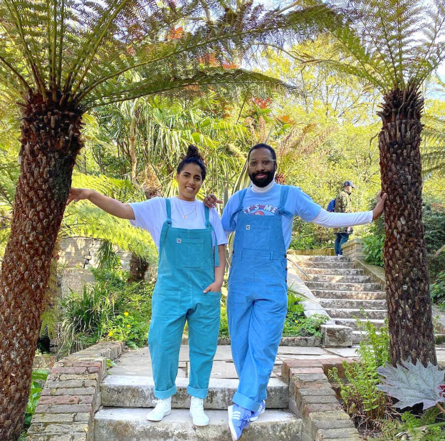 Black husband and Pakistani wife pose in matching outfits leaning against palm trees