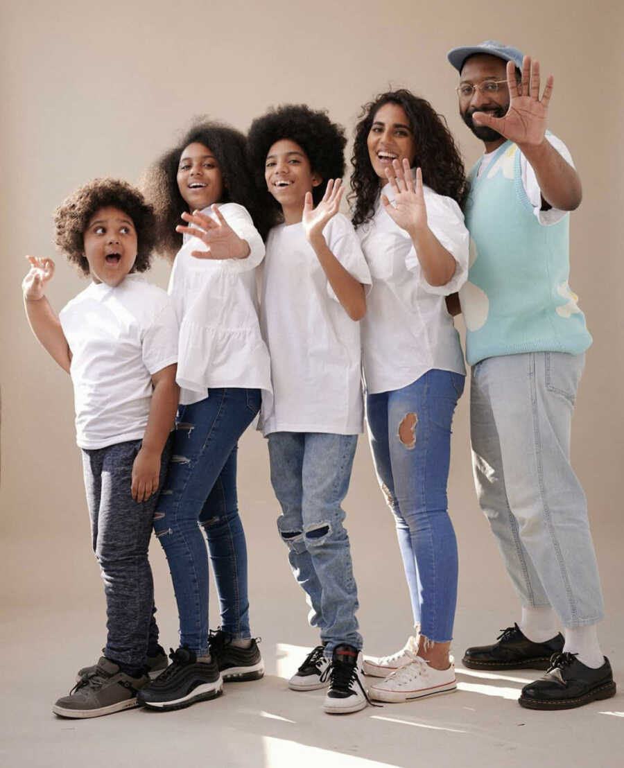 mixed race family stands from youngest member to oldest member all of them have their hand stretched out holding 5 fingers up