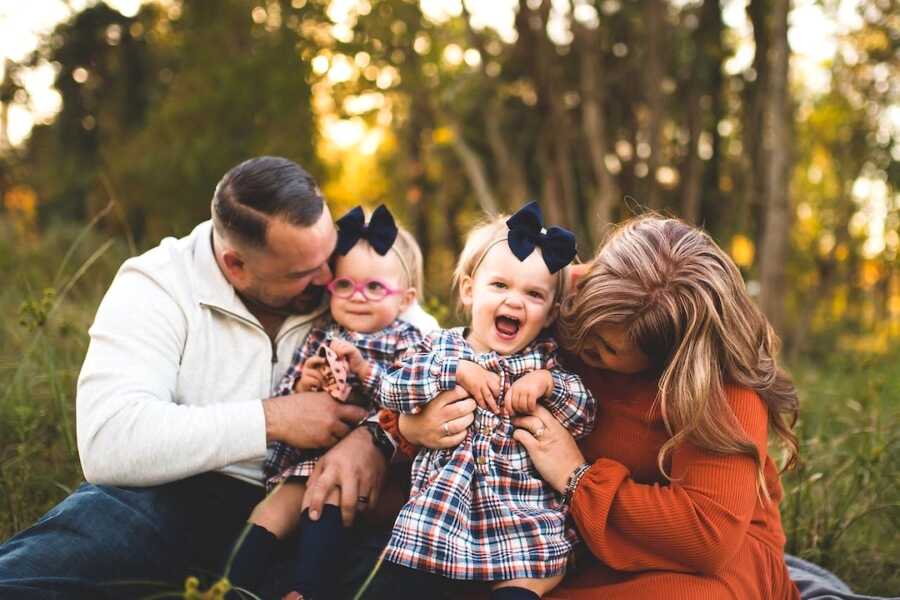 mom and dad hold their twin daughters close, they are laughing