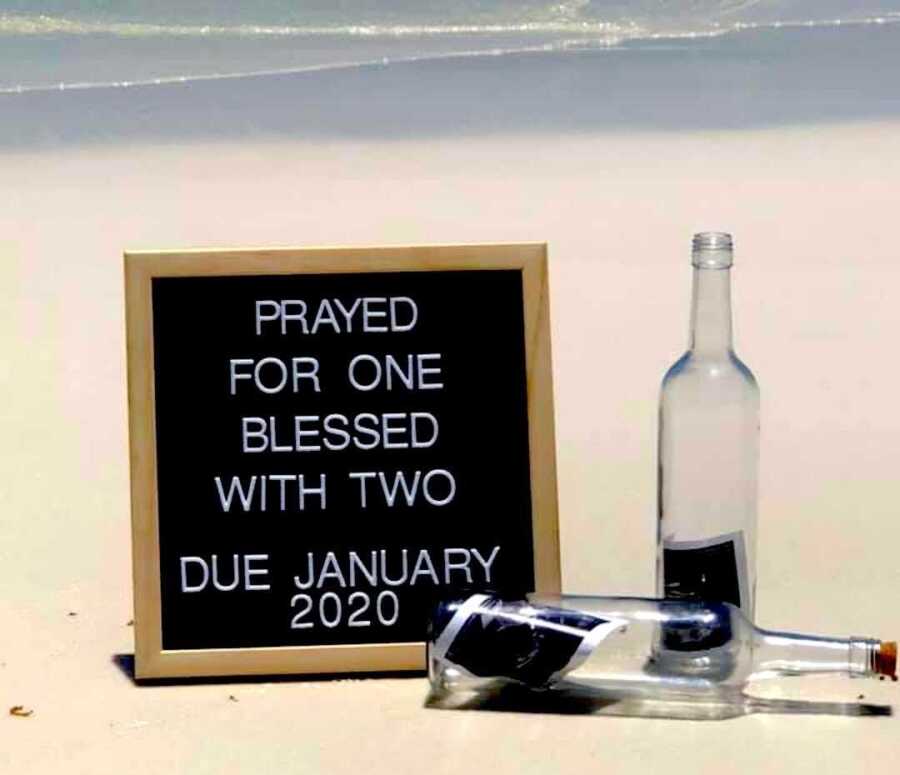 pregnancy announcement on the beach, sign reads "prayed for one blessed with two due January 2020"