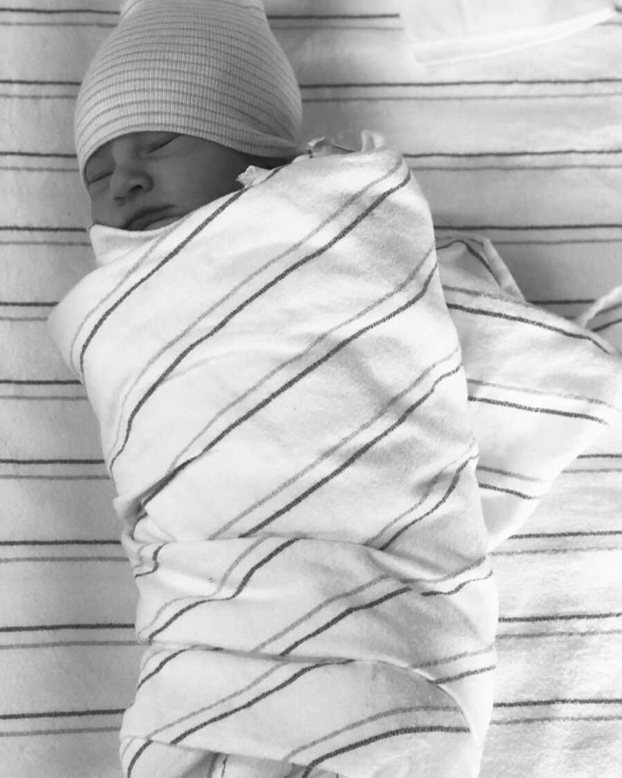 newborn baby lays swaddled in a blanket with a hat on