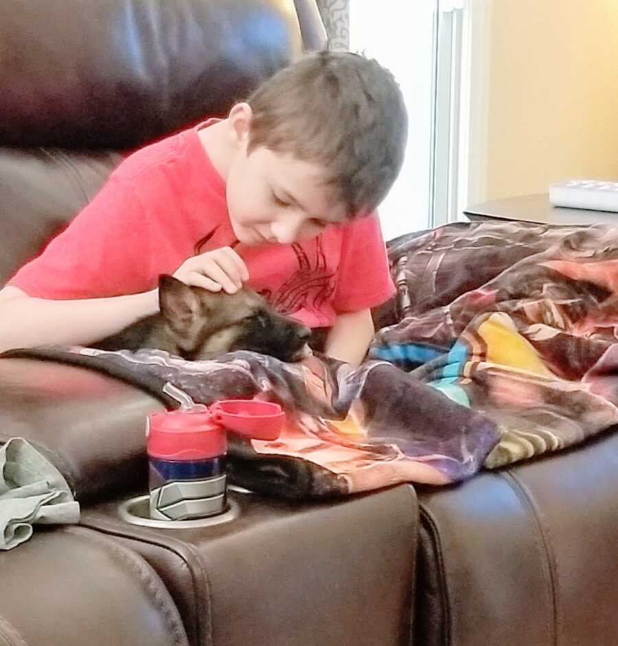 Boy with Duchenne sits on the couch, cuddled up with a puppy