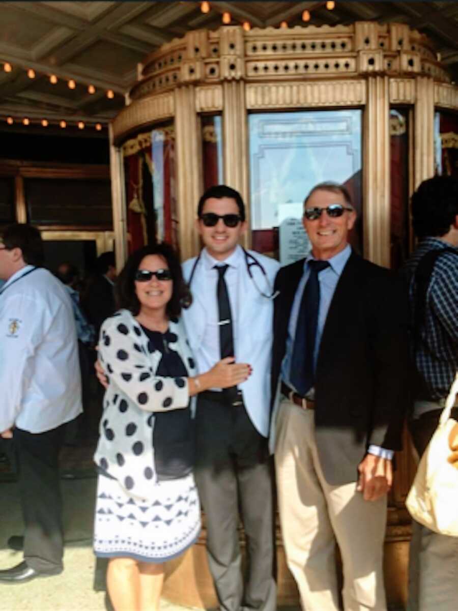 man poses with parents at his white coat ceremony for medical school