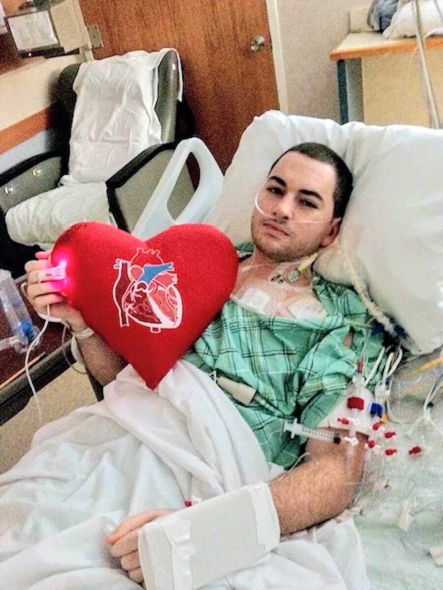 man holds a heart shaped pillow after his heart transplant surgery