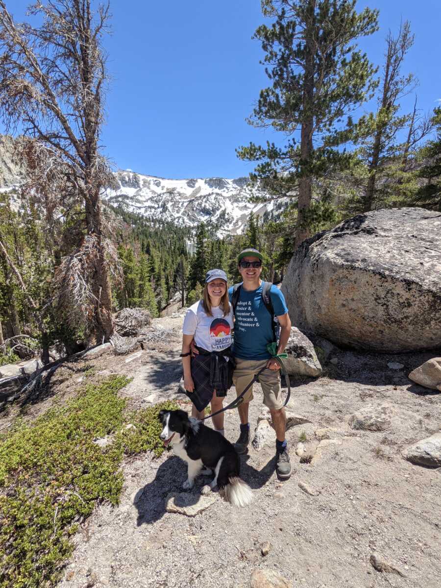 Happy couple takes picture together in the mountains with their dog.