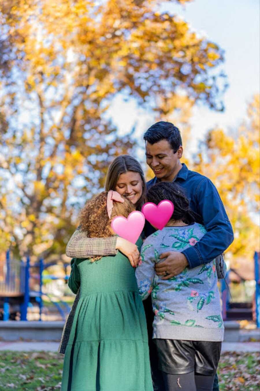 young foster parent couple hug foster daughters