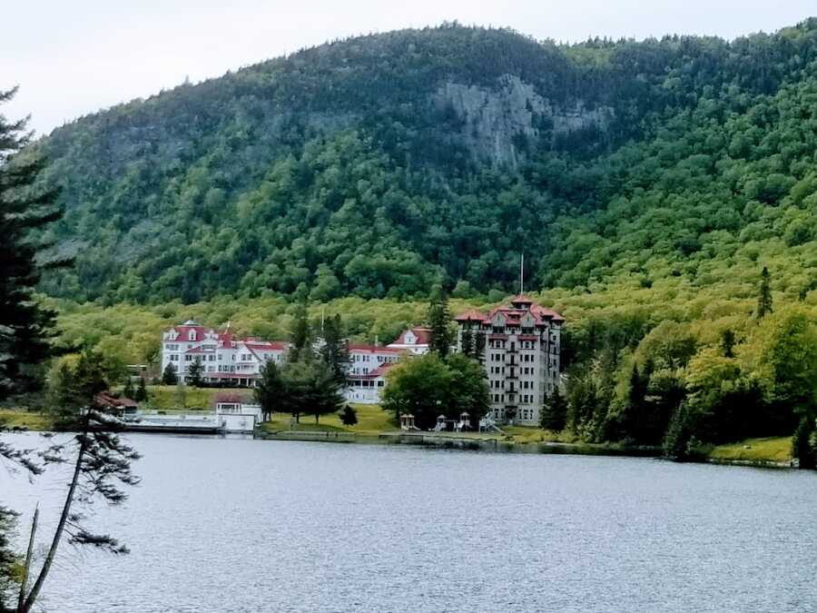 The Balsams hotel from across the water, mountains covered in trees rest behind the building