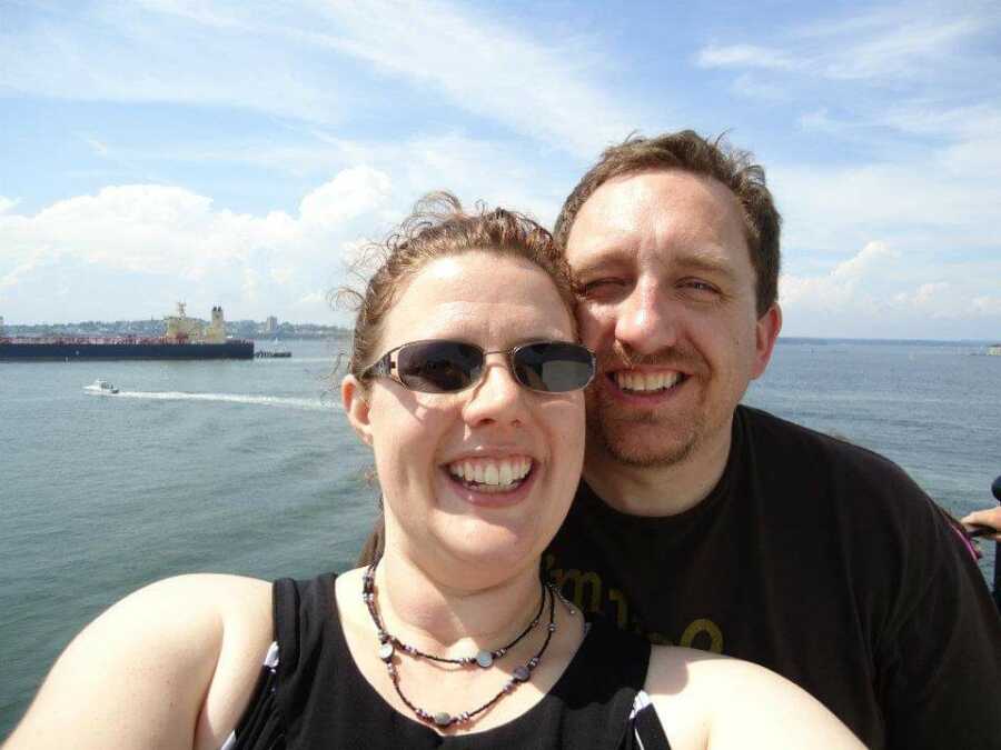Couple takes selfie together with water and boat in the background.