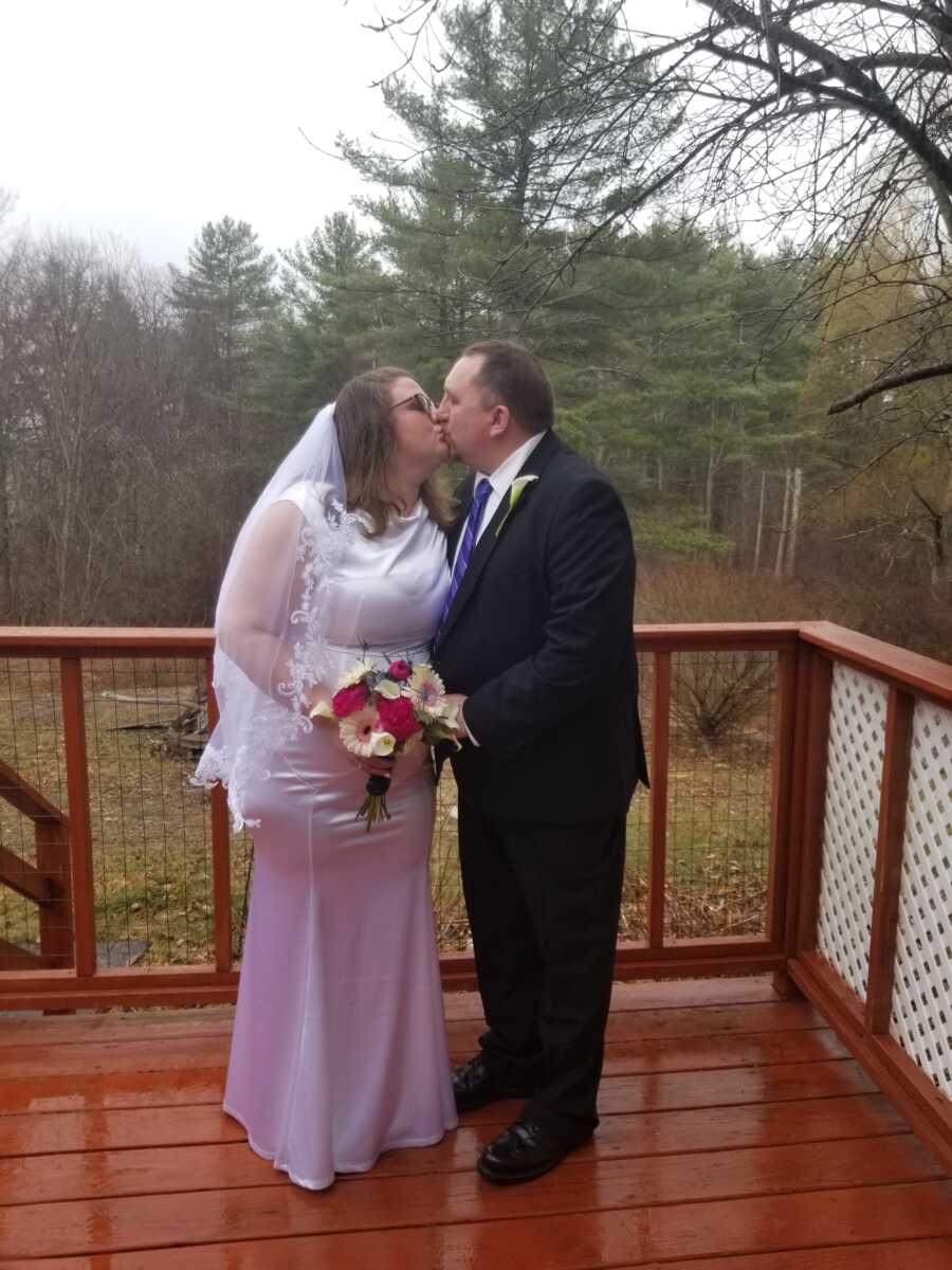 Bride and groom kiss on porch overlooking beautiful outdoor landscape.