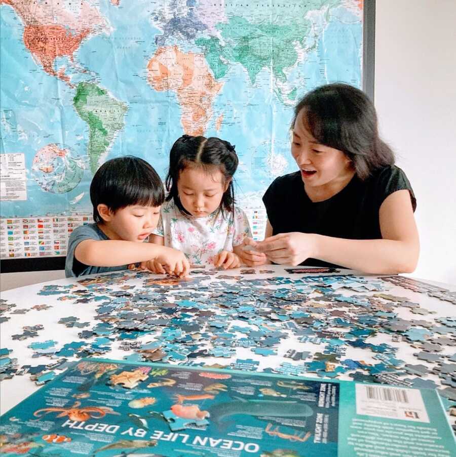 A stay-at-home mom helps her two young children with a large puzzle