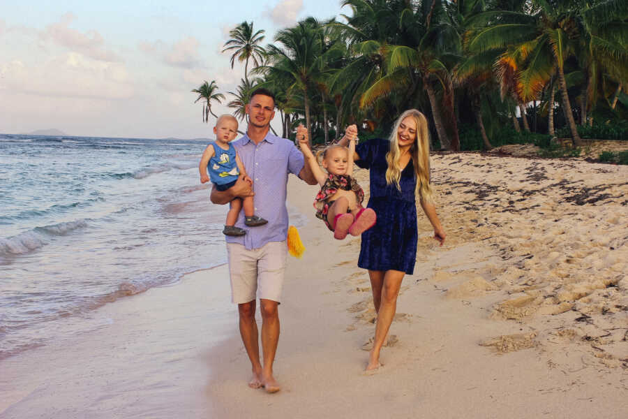 parents walk on the beach while holding their two children, a son and daughter