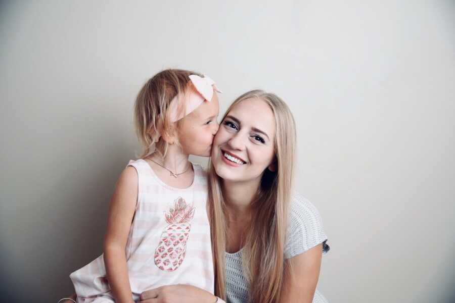 mother sits next to her daughter while the girl kisses her cheek, mom smiles