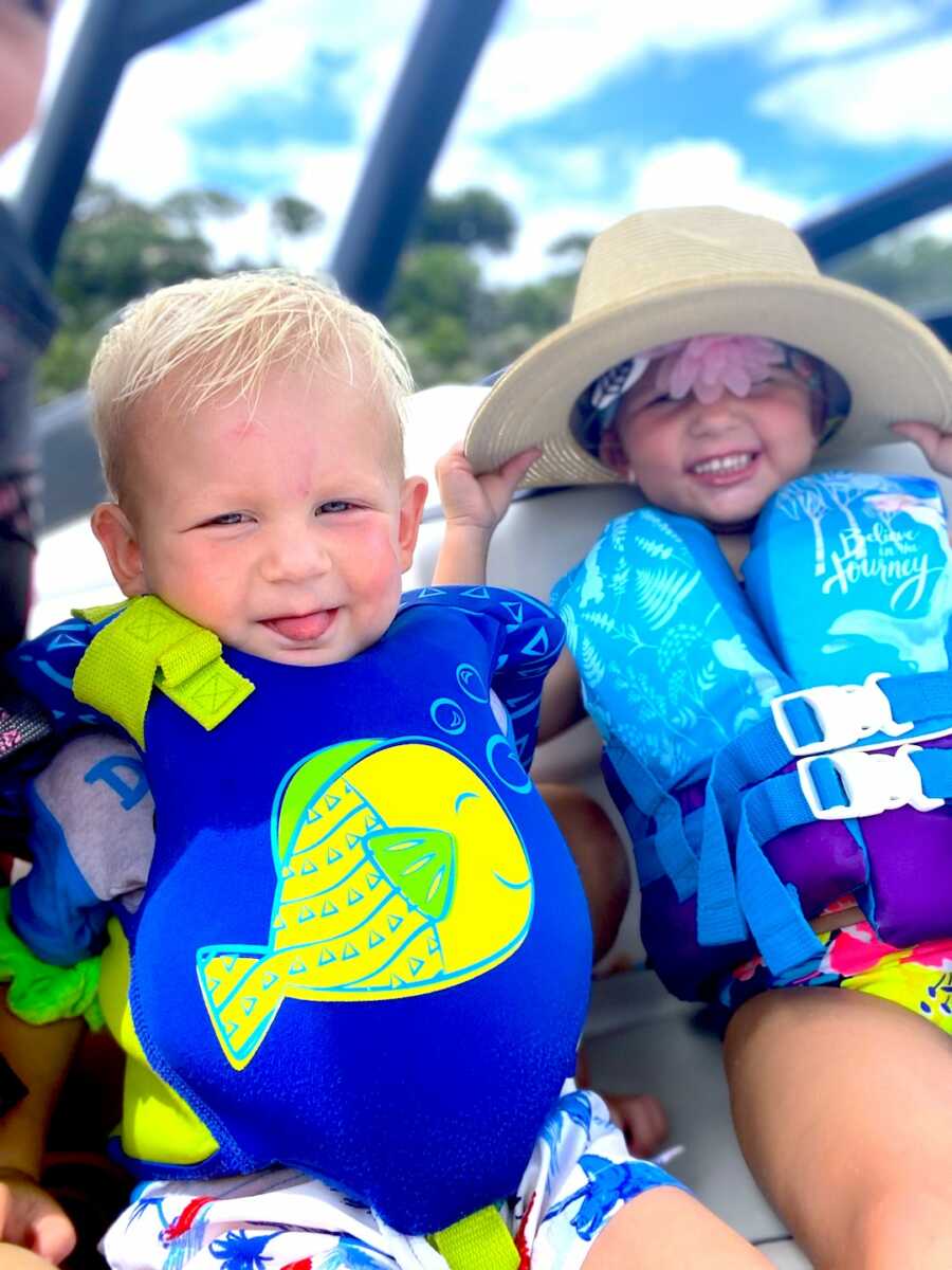 siblings, brother and sister, sit on a boat with life jackets on