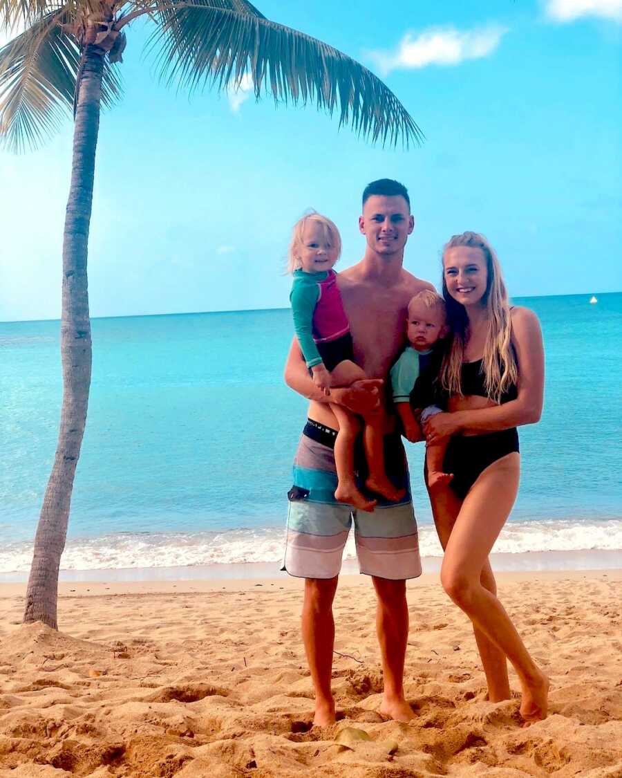 mom and dad hold their son and daughter while standing on the beach in front of the ocean