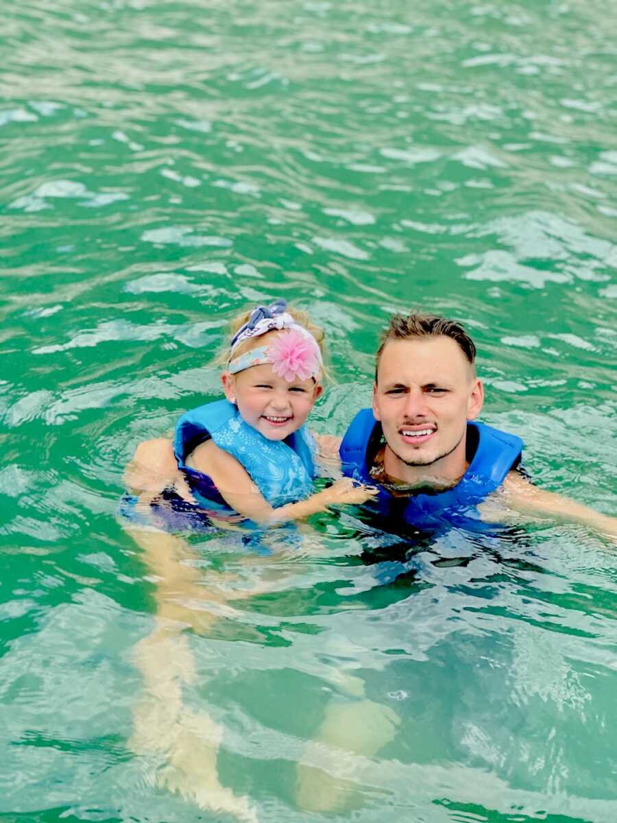 dad floats in the water while holding his daughter at his side