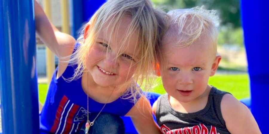 siblings, brother and sister, sit on the playground and pose for a picture