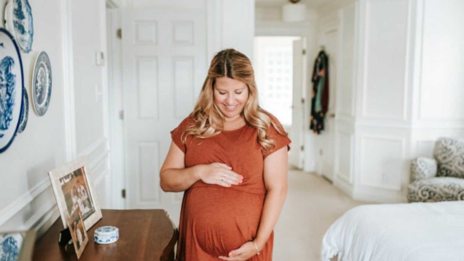 Pregnant woman in an orange dress cradling her belly