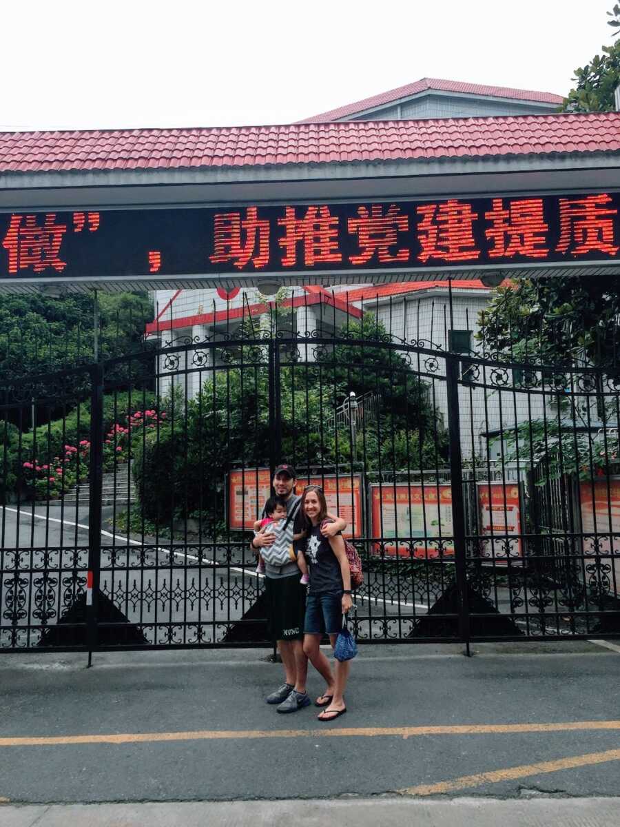 adoptive parents stand in-front of a Chinese landmark while holding their adopted baby