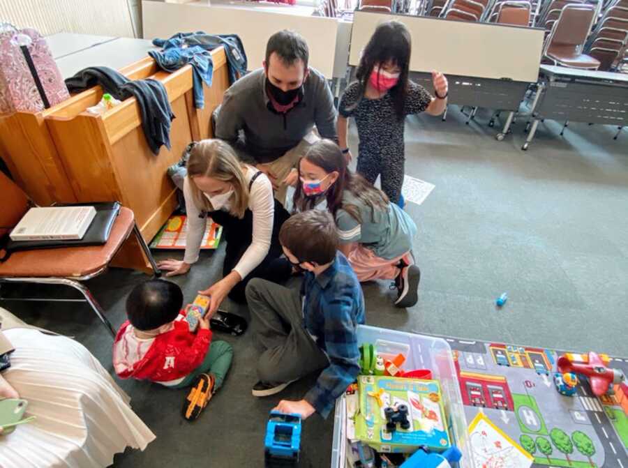 adoptive parents play with toys with their two biological children, and two adopted children