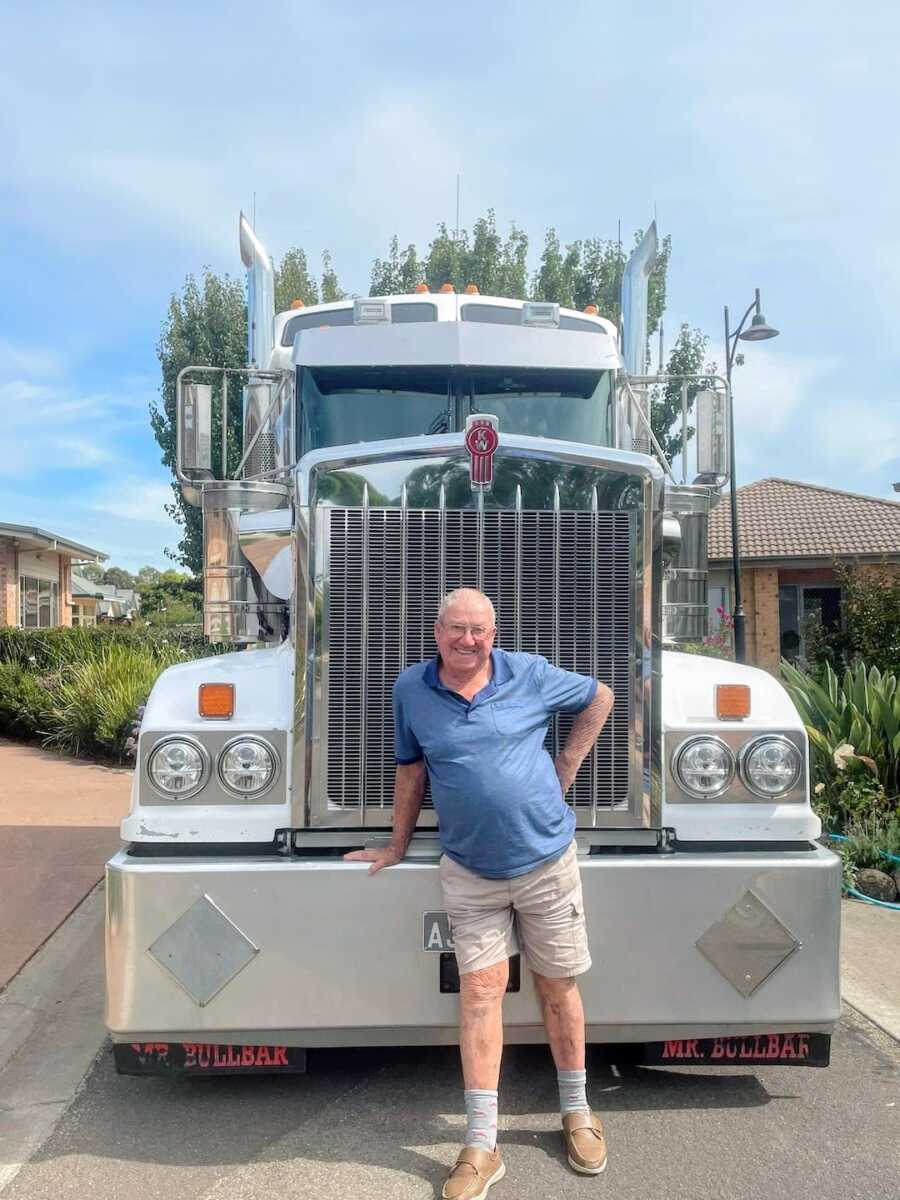 man stands in front of big rig smiling widely