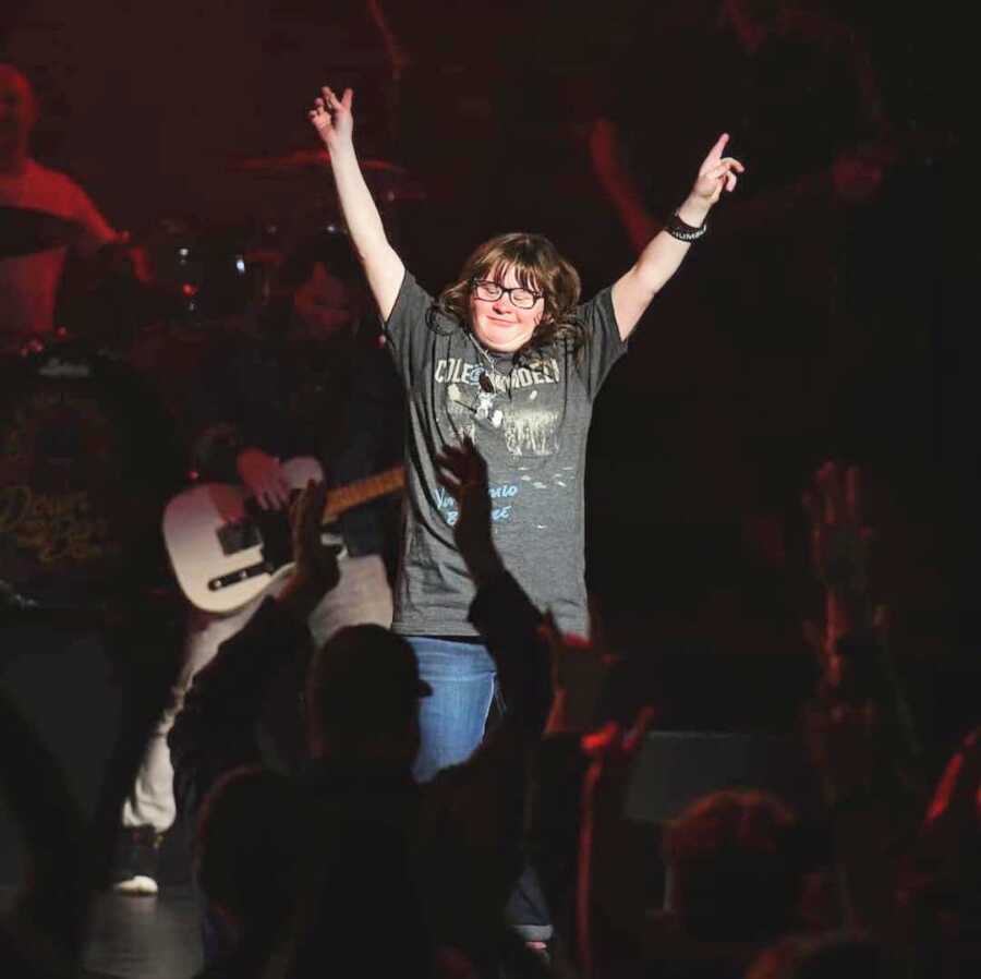 young girl on stage at a Cole Swindell concert raises her arms up to the music