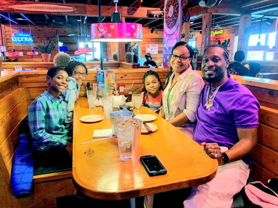 blended family, parents and three children, sit at a booth in a restaurant