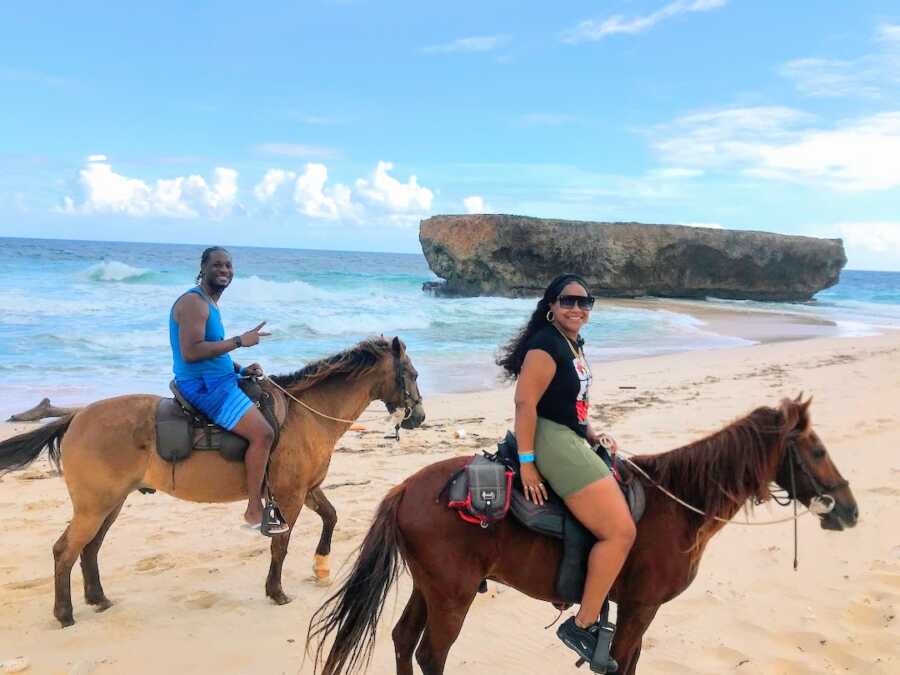 husband and wife ride horses together while on the beach