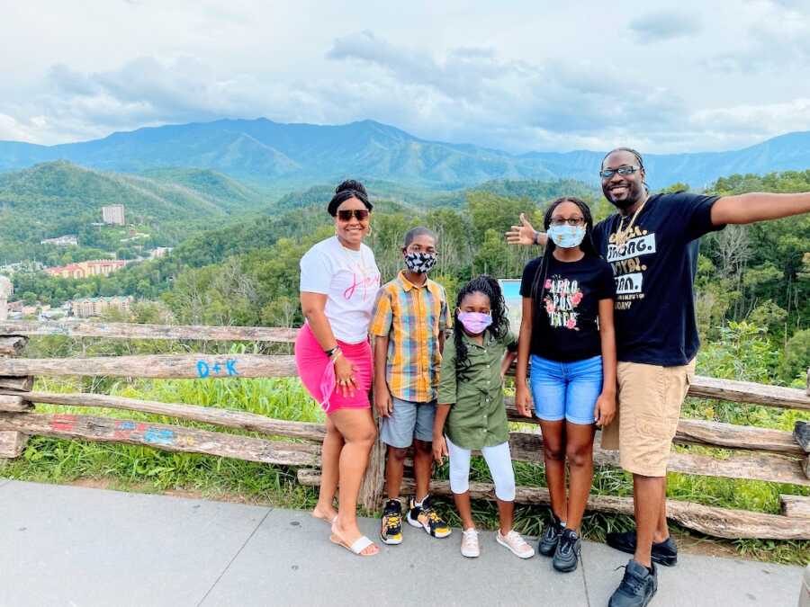 blended family stands together in front of a scenic view, parents and three children