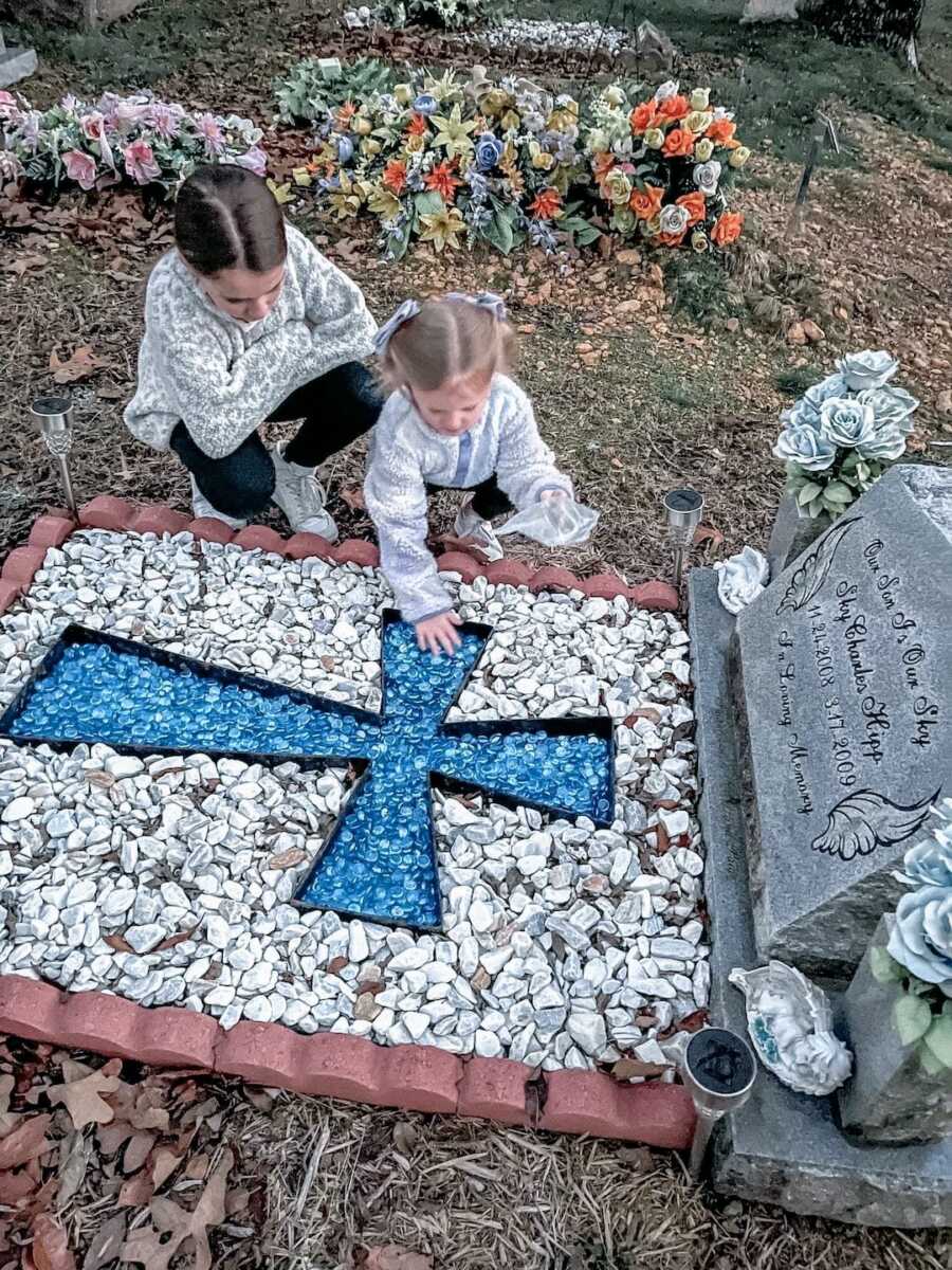 the two sisters of a boy who died from S.I.D.S. sit at their brothers grave