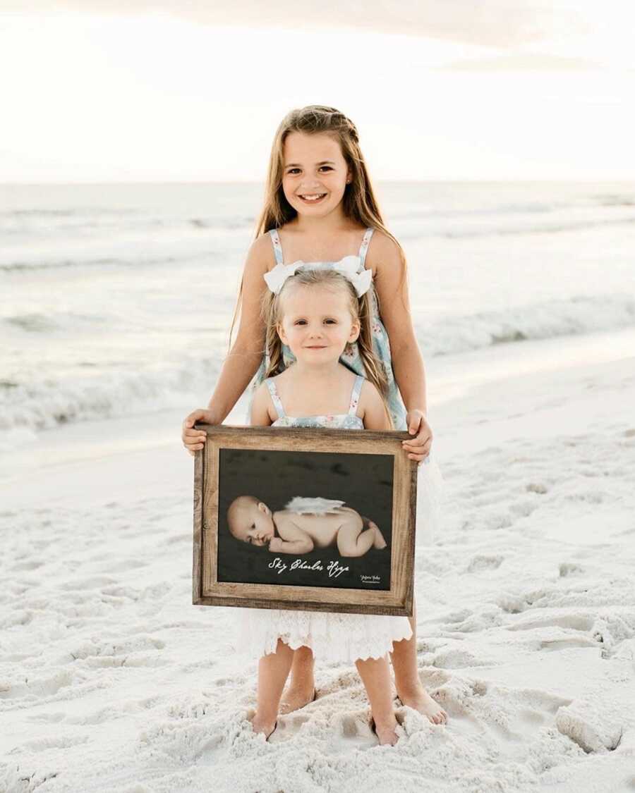 two daughters hold an image of their brother who has passed away from S.I.D.S.