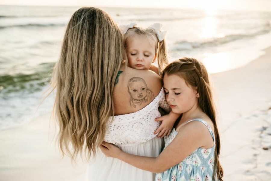 mother holds one daughter while the other wraps her arms around her mom