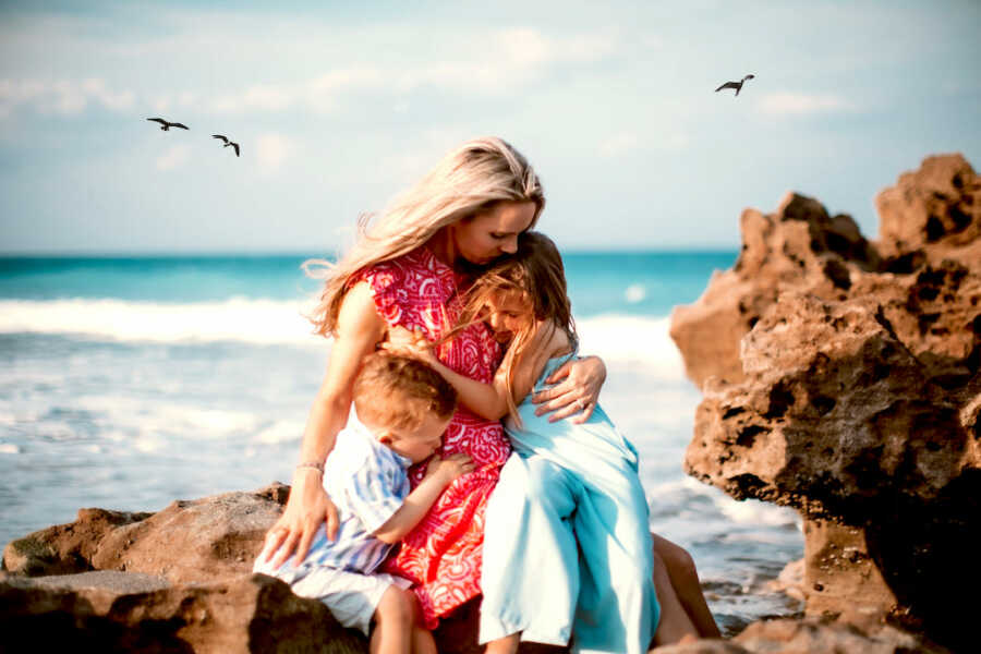 mother with autoimmune diseases holds her two children close to her while at the beach