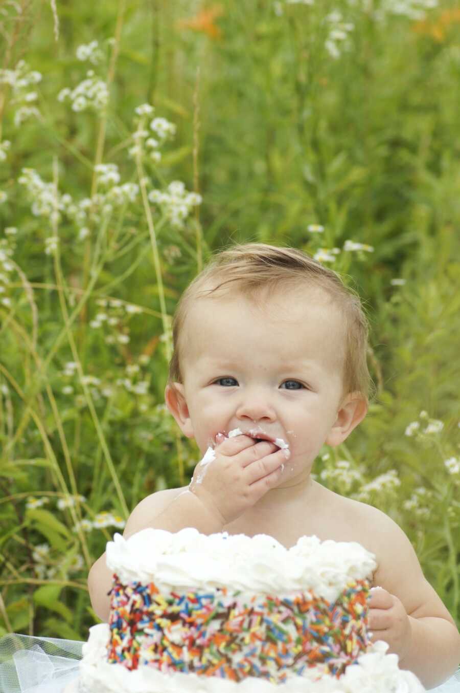 baby sits in front of a cake and eats it with it's hands