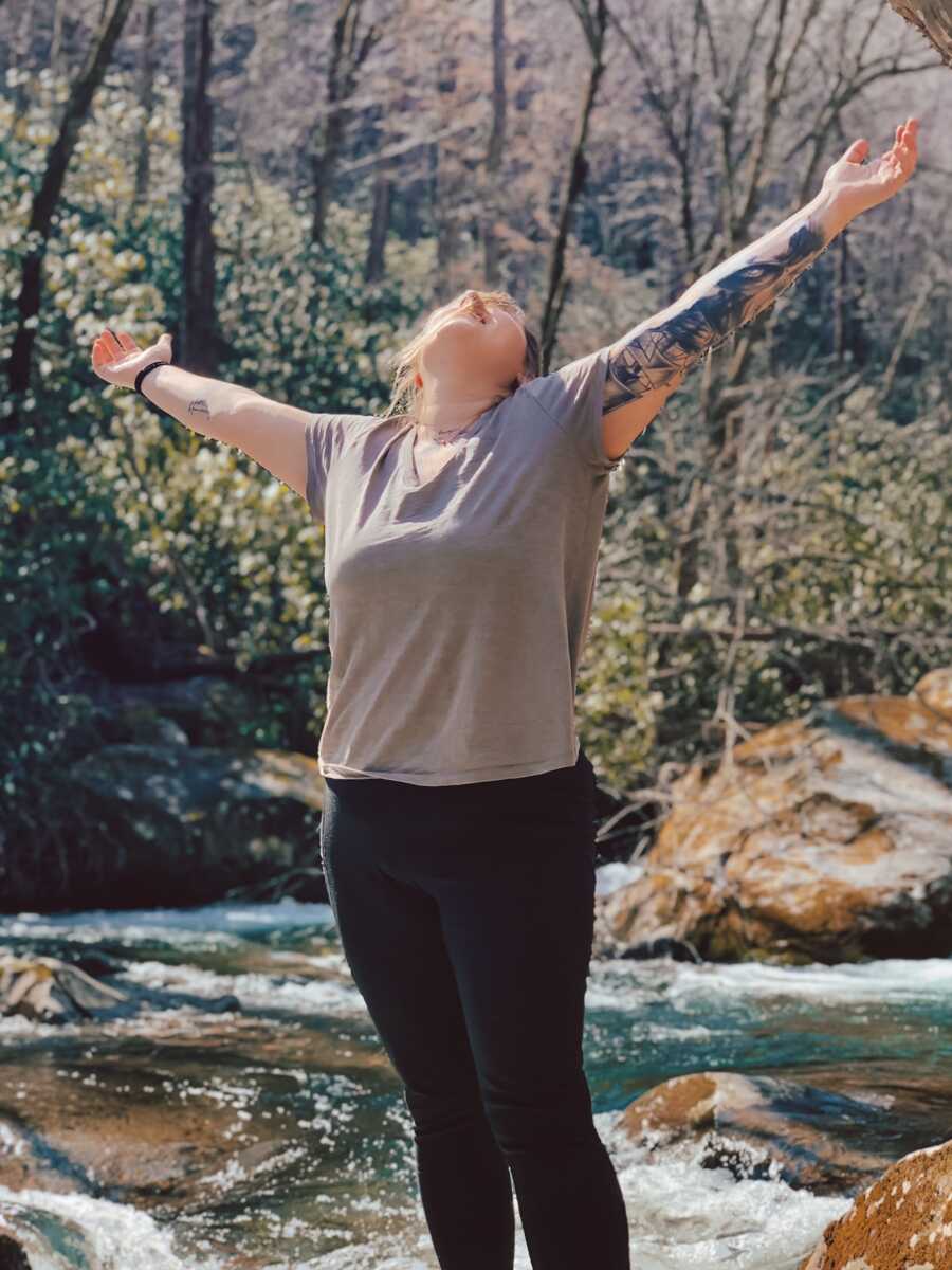 birth mom stands with nature, looks up to the sky with her arms out