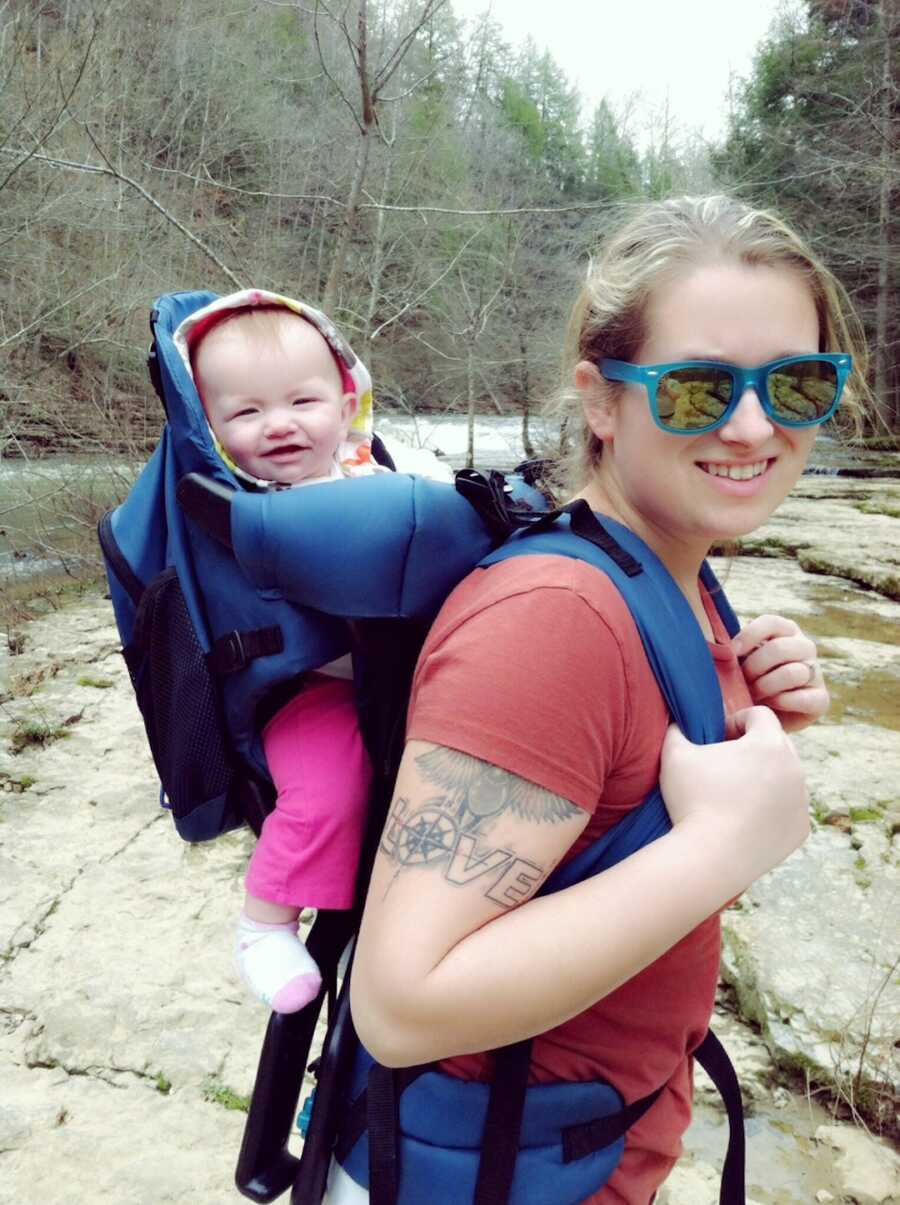 mom holds her young baby girl on her back in a backpack back