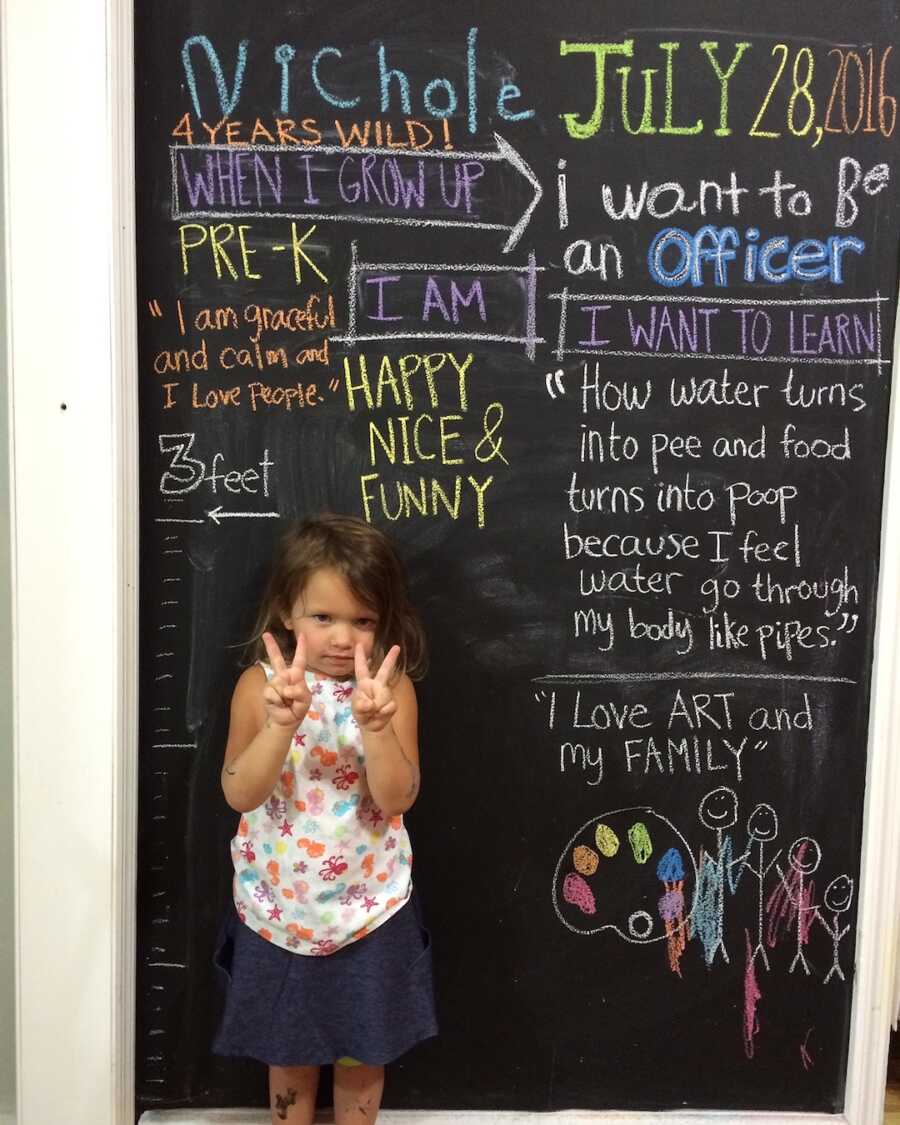 young girl stands in front of chalkboard that is decorated for her birthday