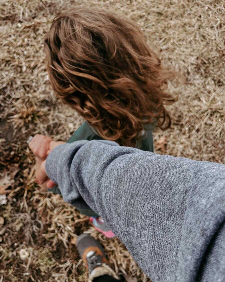 Foster mom wearing gray sweatshirt holds foster child's hand. 