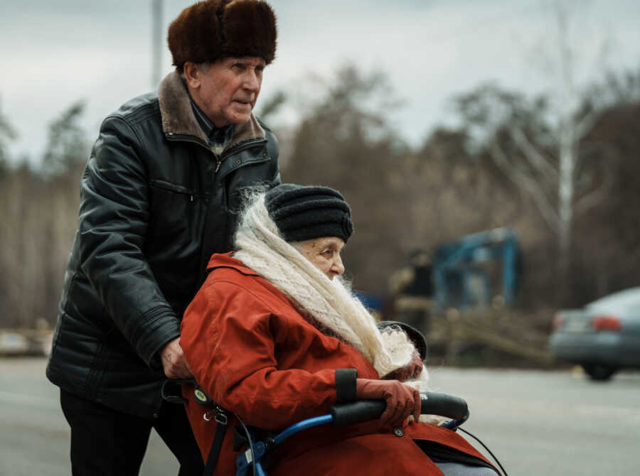 Elderly man pushes woman in wheelchair to evacuate.