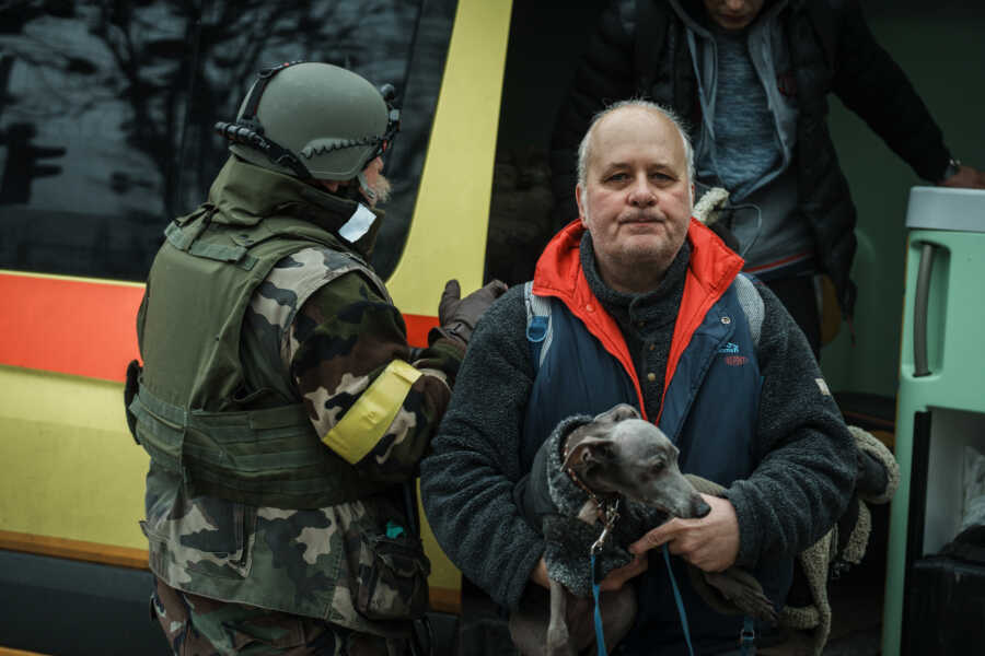 Man holds dog waiting to board bus for evacuation.