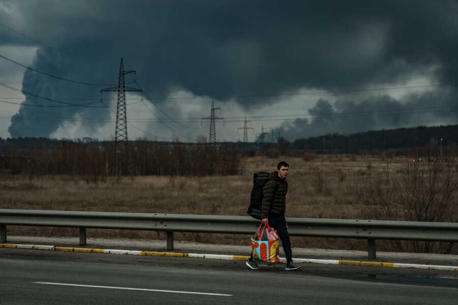 Ukrainian walking on highway with giant clouds of smoke behind them.