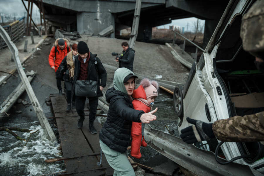 Young women carrying baby reaches for hand for help.