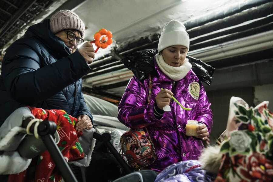 Ukrainian parents in bunker try to feed and entertain young baby.