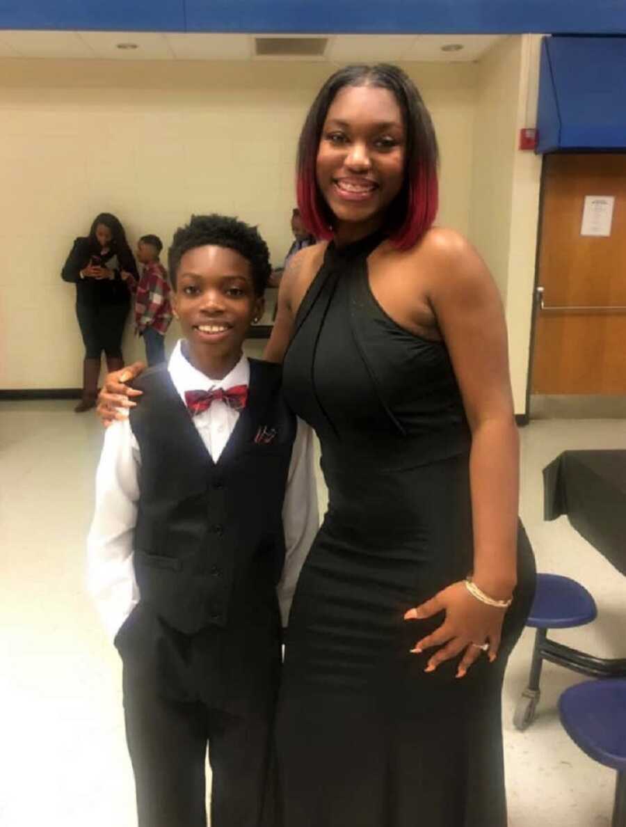 Single mom in black dress stands with arm around son in formal wear with red bow tie.