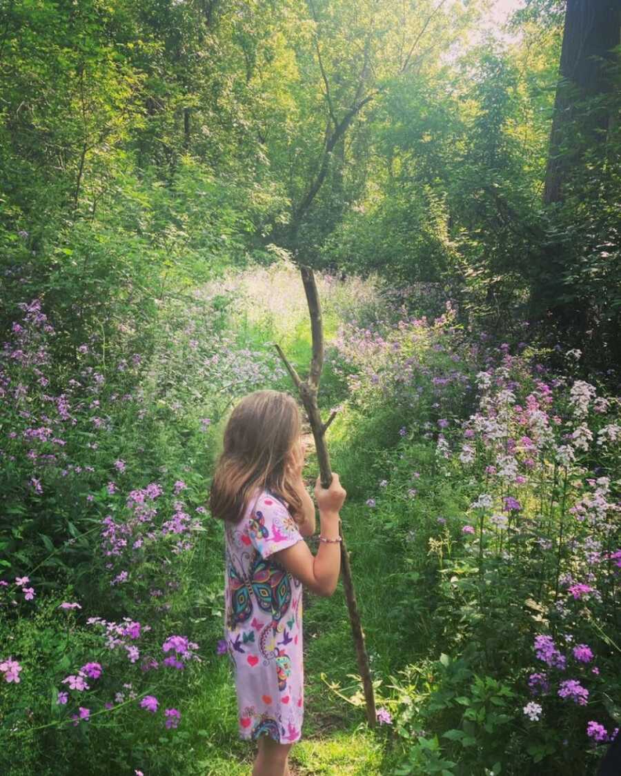 little girl with a stick in the forest exploring 