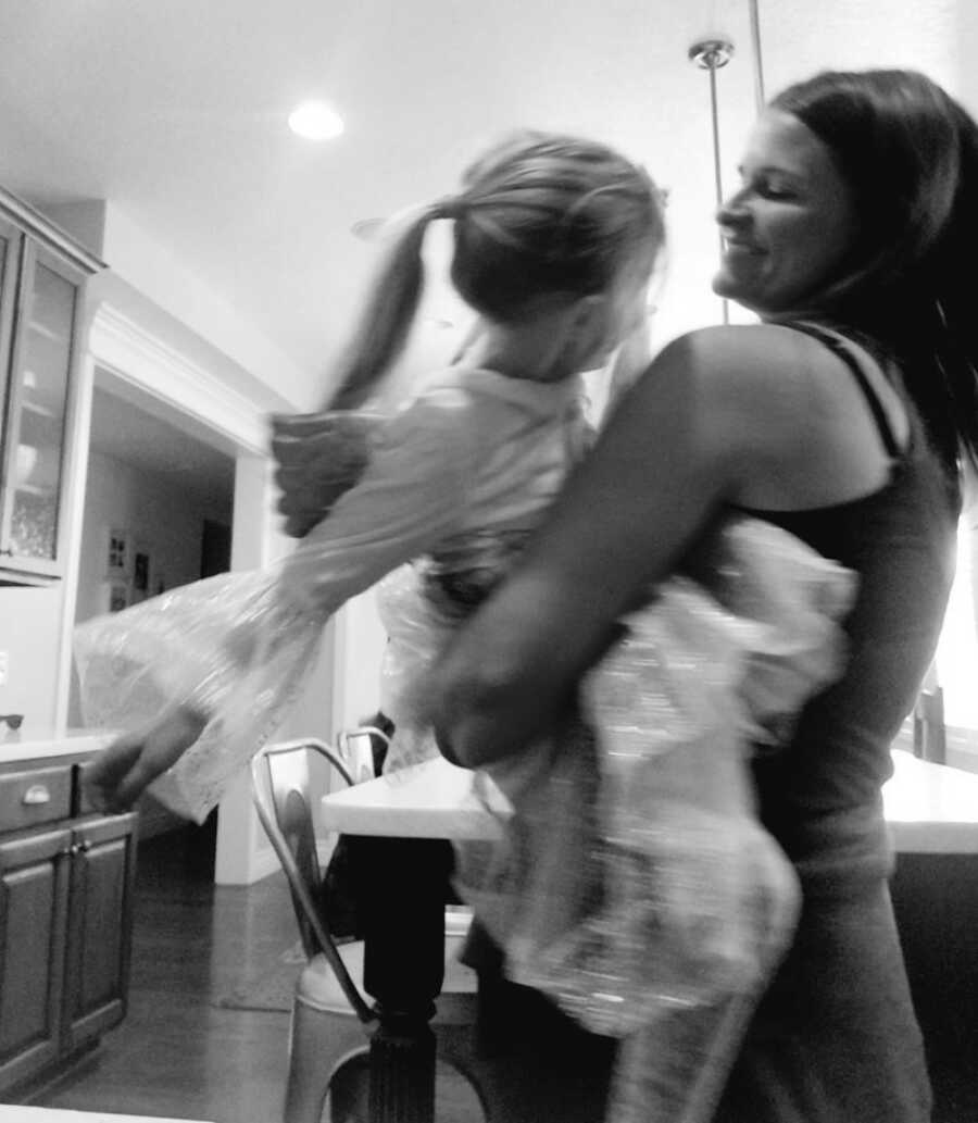 woman holding her daughter while dancing in the kitchen