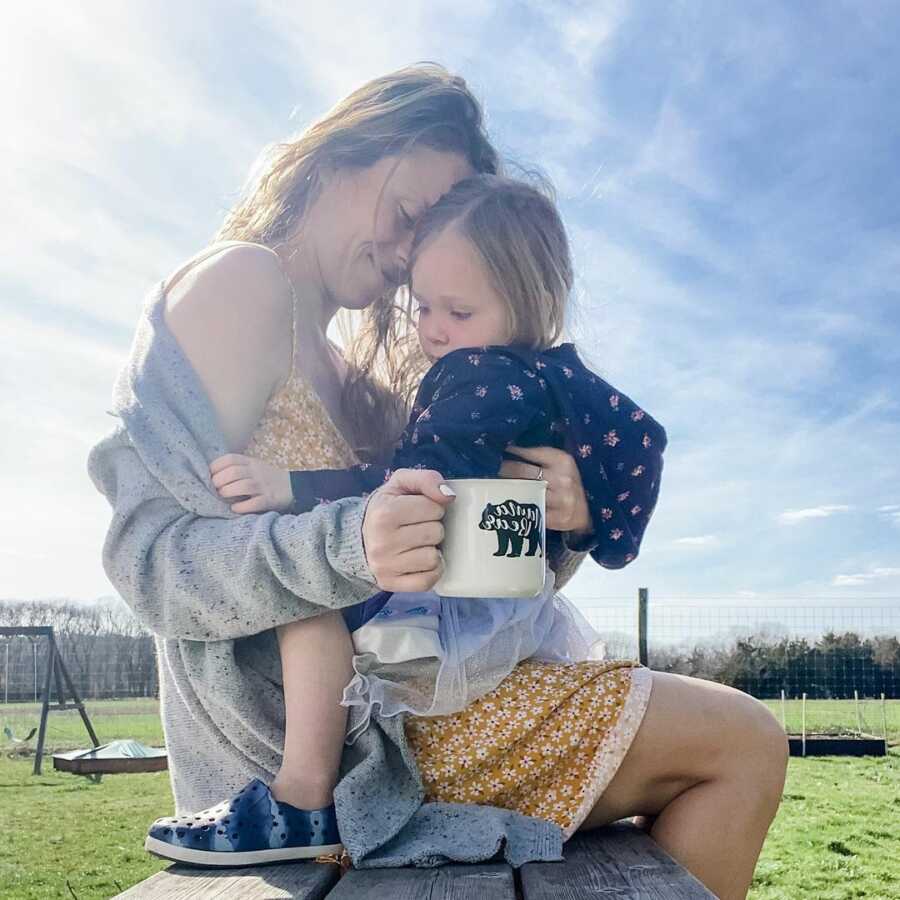 mom holding her daughter close smiling in the sunshine