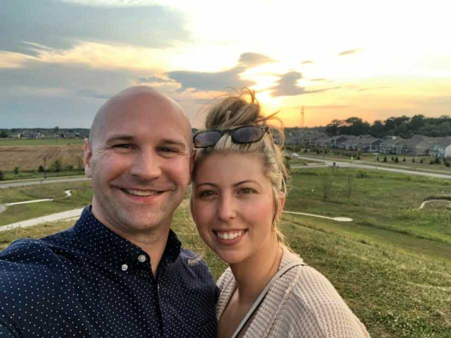 Couple take a selfie with the sun setting behind them while on a hike together